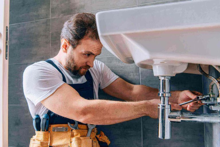 focused male plumber in working overall fixing sink in bathroom 768x513
