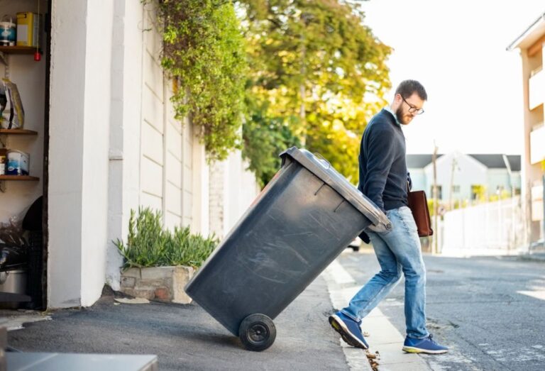 Man pulling a wheeled dumpster out of his garage while going to work 768x523
